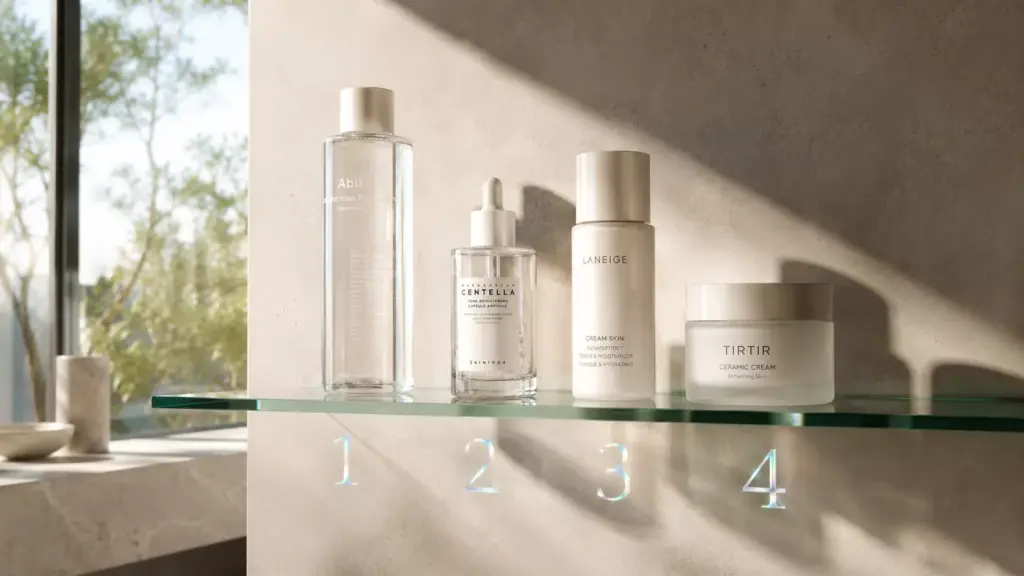 The Ultimate Skincare Routine Order: How to Layer Your Products for Maximum Glow 2 A neat horizontal lineup of luxury skincare bottles on a glass shelf, illustrating the correct molecular weight skincare routine order from thinnest to thickest.